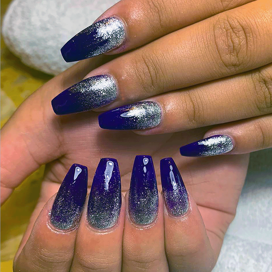 Hands with long almond-shaped acrylic nails in pink and purple glitter, one pink nail featuring a black heart design.
