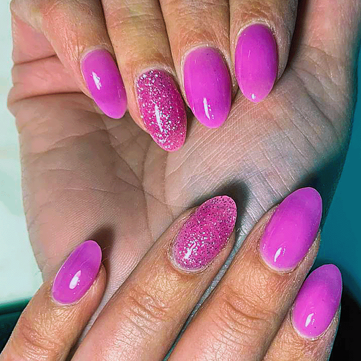 Hands with almond-shaped nails painted in bright pink, with two nails featuring pink glitter accent.
