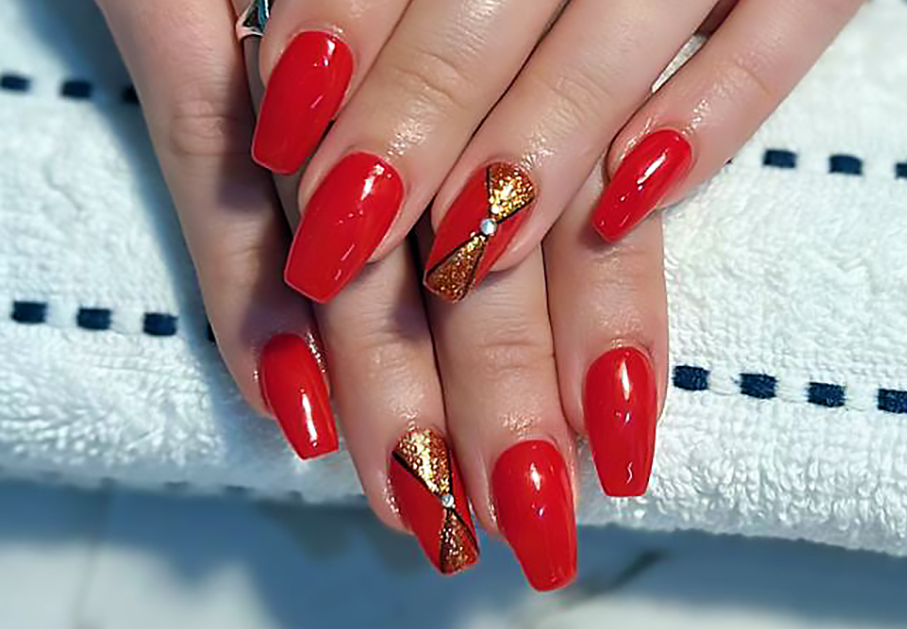Close-up of hands with long red manicured nails featuring gold glitter and a small rhinestone on two nails.