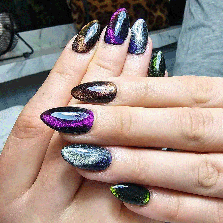 Hands with long almond-shaped nails featuring shiny, multicolored chrome gradient nail polish in purple, gold, silver, and green hues.