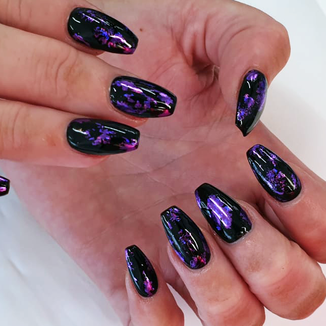 Hands with black glossy nails featuring purple and pink marbled nail art.